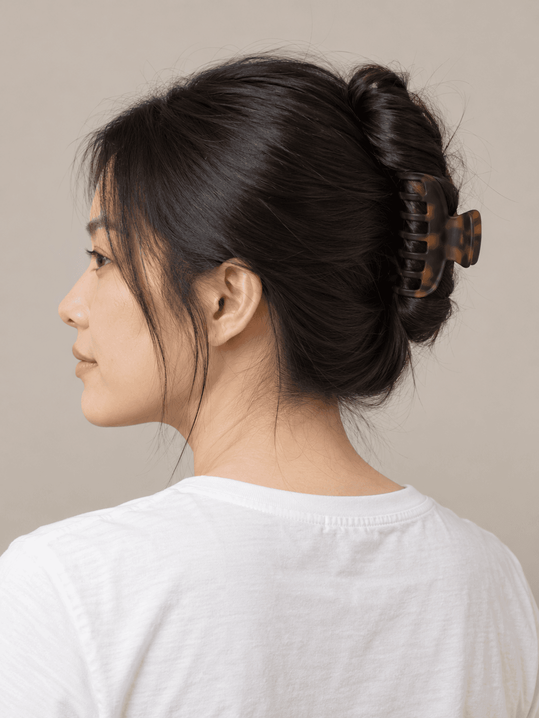 Claw-clip twist on a woman with light skin and straight black hair, seen from the back-left to show the style