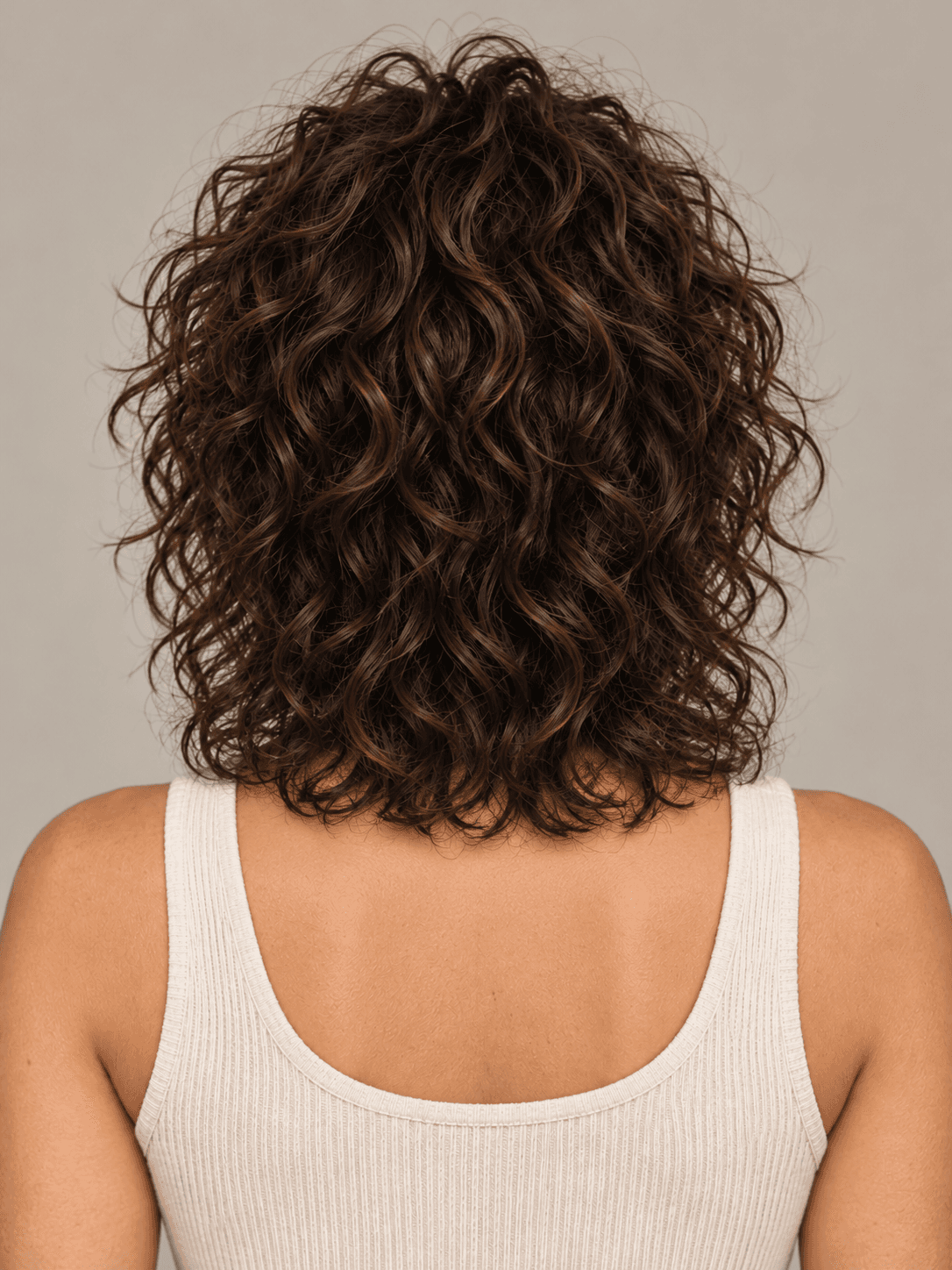 Curly shag hairstyle with curtain bangs on a woman with dark brown curly hair, back view