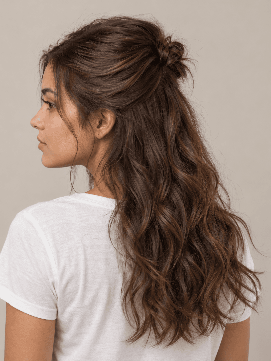 Half-up half-down style on a woman with light brown skin and wavy chestnut hair, seen from the back-left to show the style