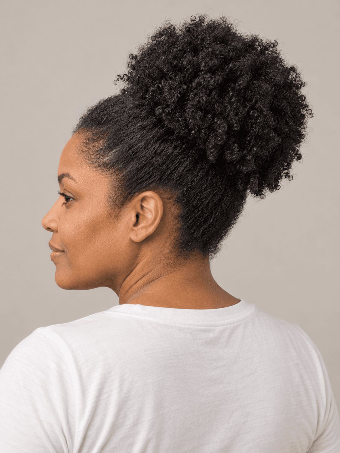 High puff on a woman with medium brown skin and coily hair, seen from the back-left to show the style