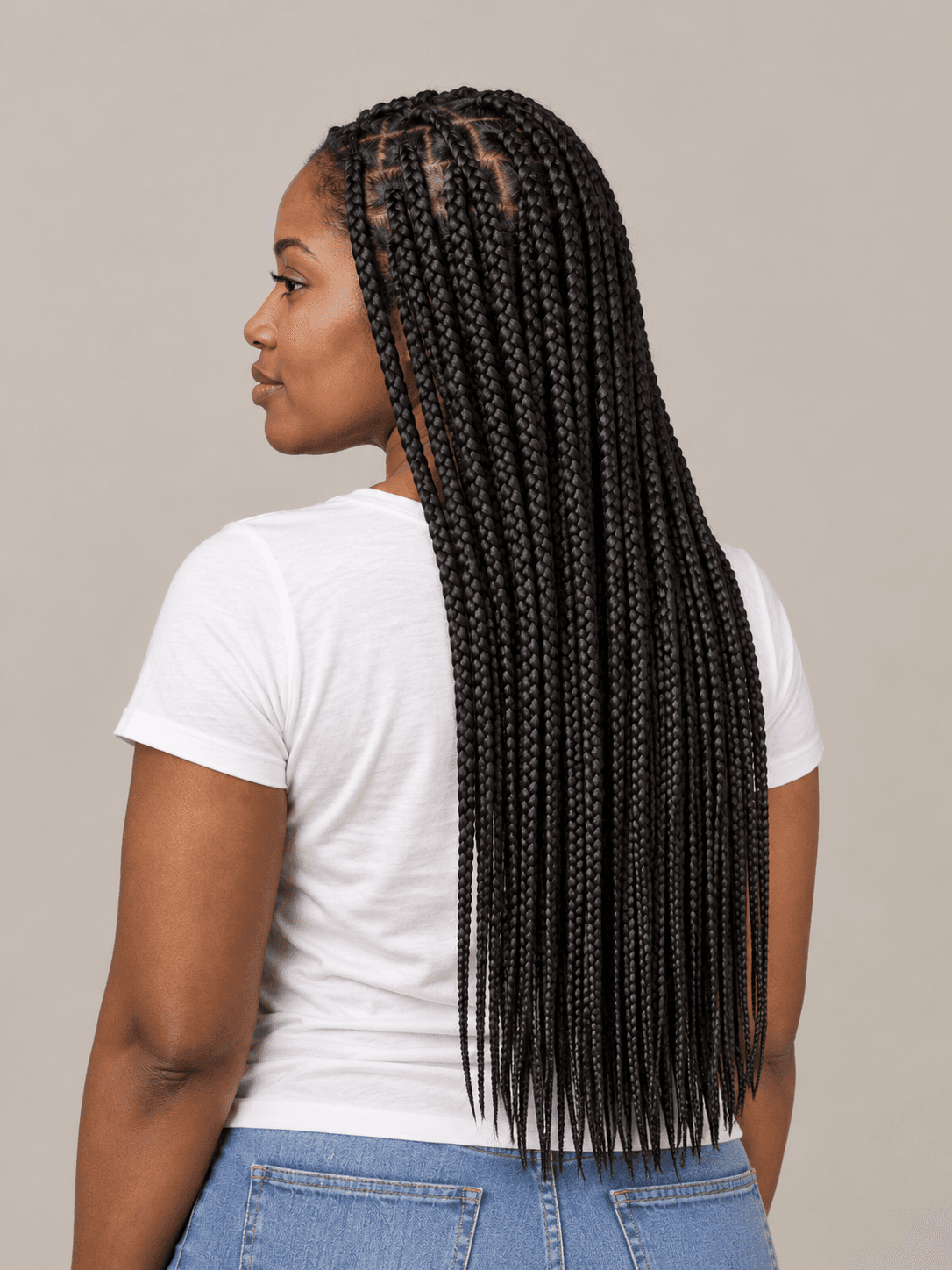 Knotless box braids on a woman with deep brown skin, seen from the back-left to show the style