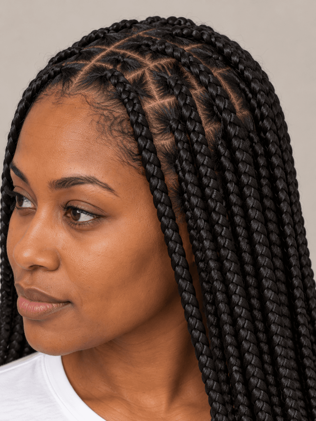 Knotless box braids on a woman with deep brown skin, close view of the parts and flat braid roots