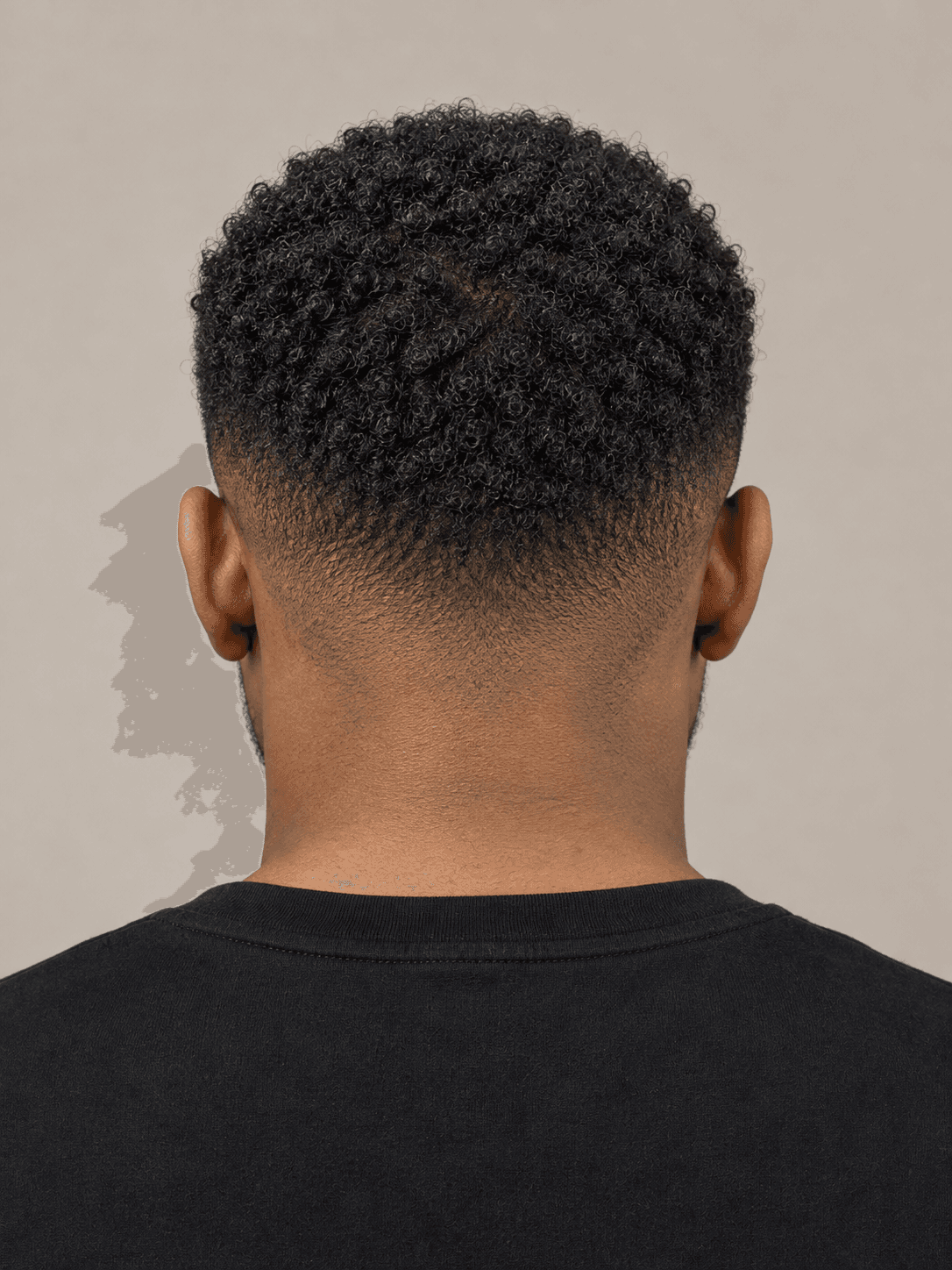 Low fade hairstyle with a curly top on a man with black coily hair and a beard, back view