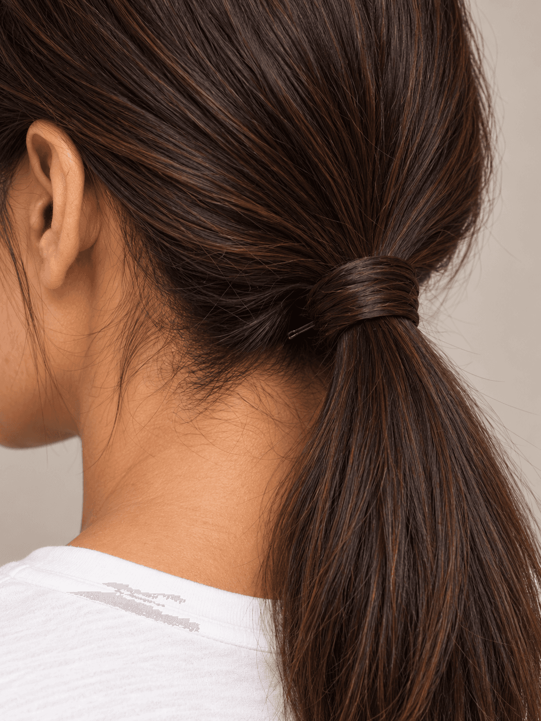 Low Ponytail with Wrapped Base on a woman with light brown skin and dark brown hair, close view of the nape and the strand wrapped round the band