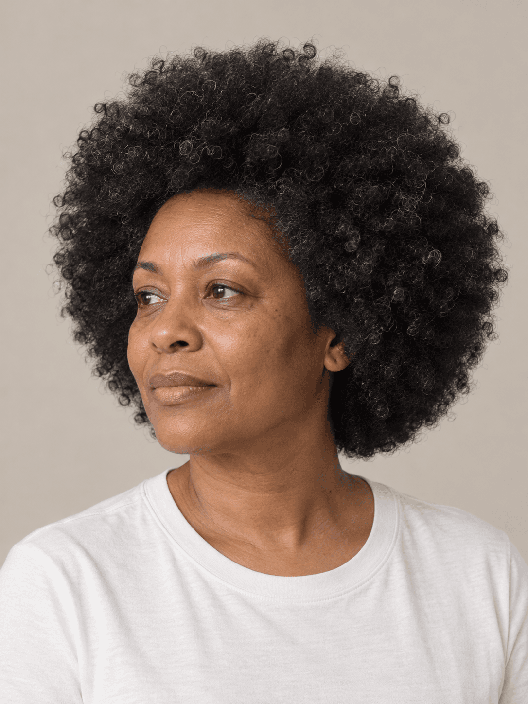 Rounded afro on a woman with medium brown skin and coily black hair with a few silver strands, three-quarter view