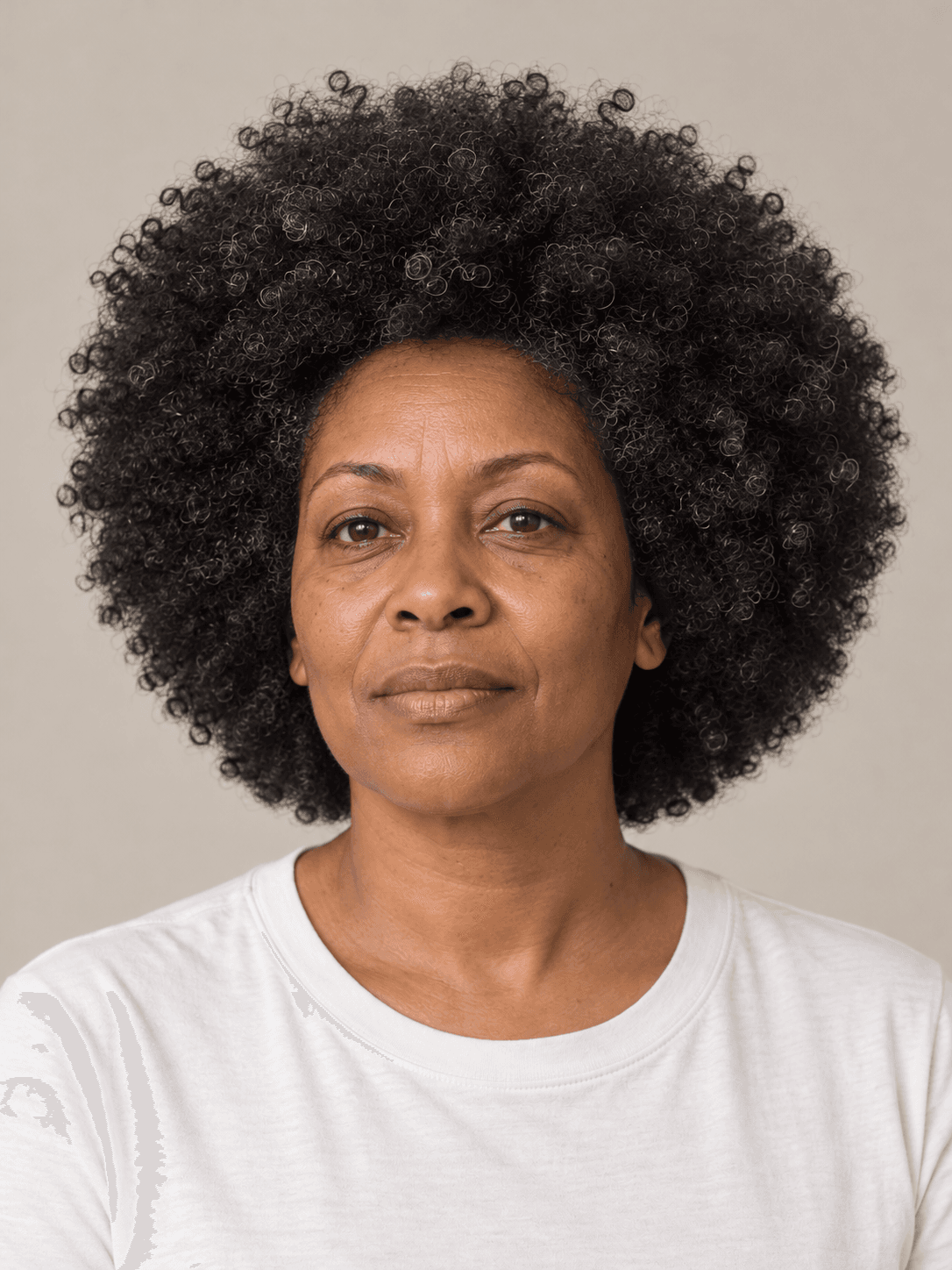 Rounded afro on a woman with medium brown skin and coily black hair with a few silver strands, front view