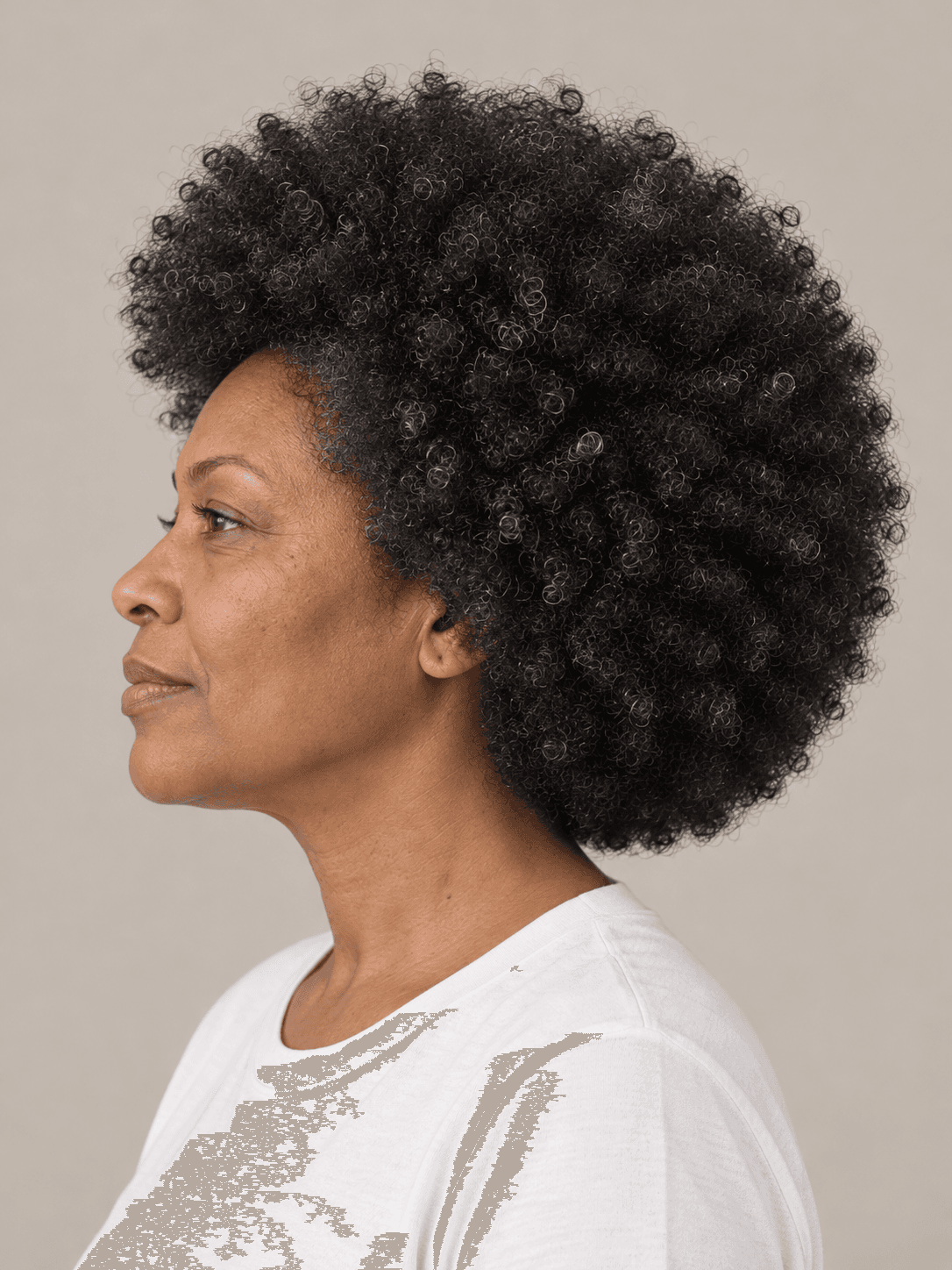 Rounded afro on a woman with medium brown skin and coily black hair with a few silver strands, side view