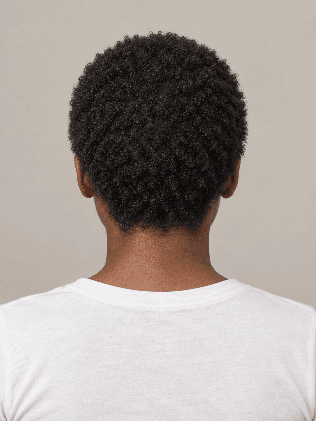 Short natural afro on a woman with dark brown skin and tightly coiled black hair, back view