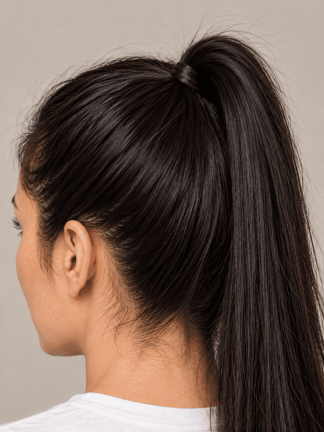 Sleek High Ponytail on a woman with light olive skin and straight black hair, close view of the base at the crown, the tie hidden under a wrapped strand