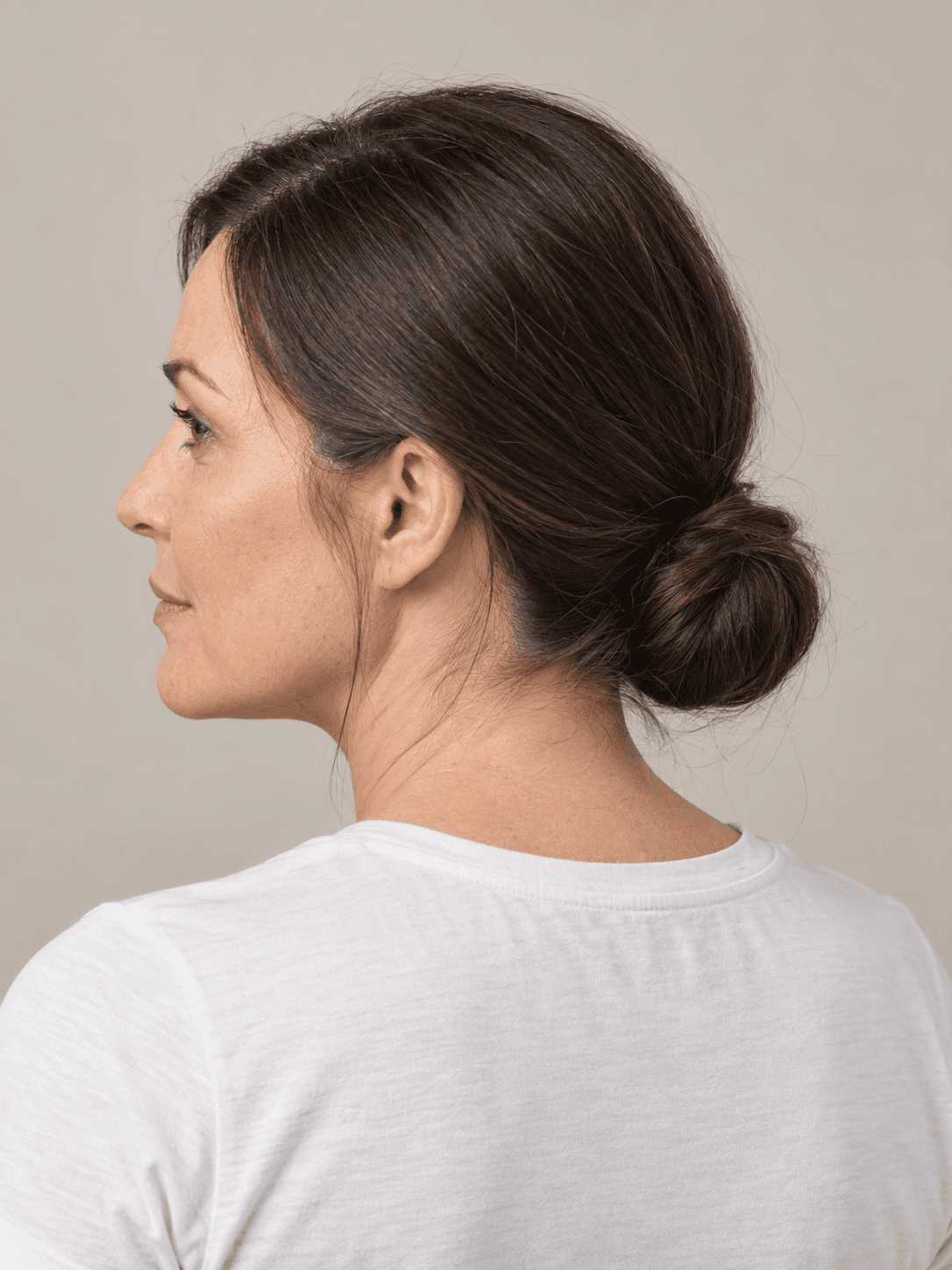 Sleek low bun on a woman with light skin and straight dark brown hair, seen from the back-left to show the style
