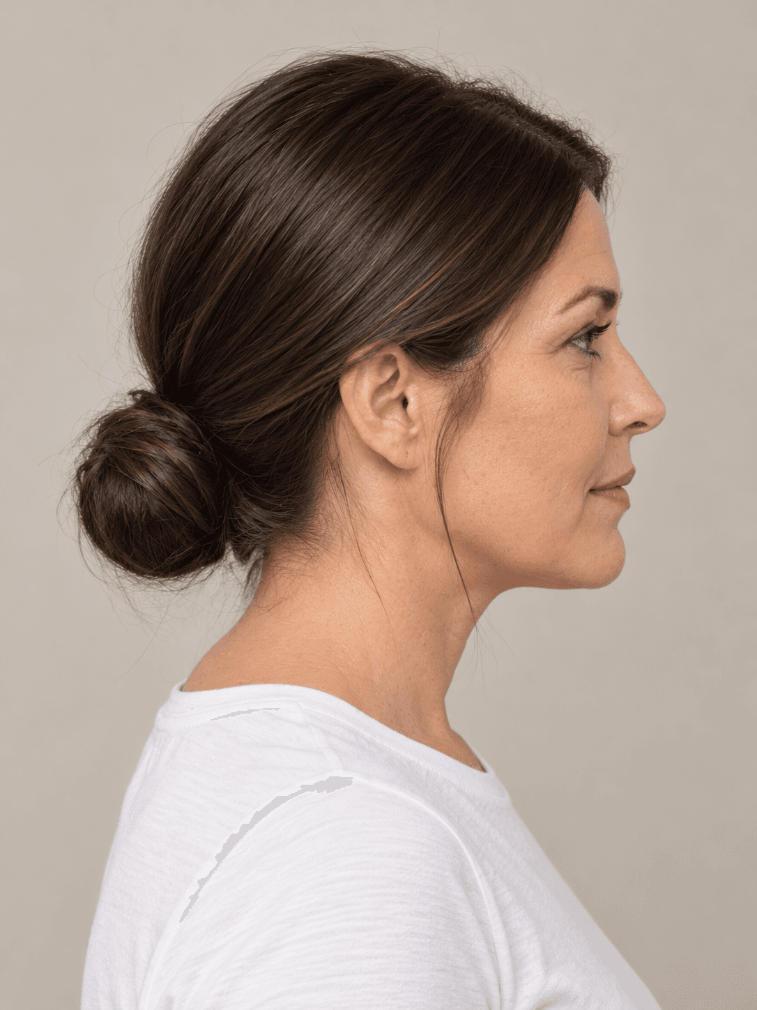 Sleek low bun on a woman with light skin and straight dark brown hair, side view