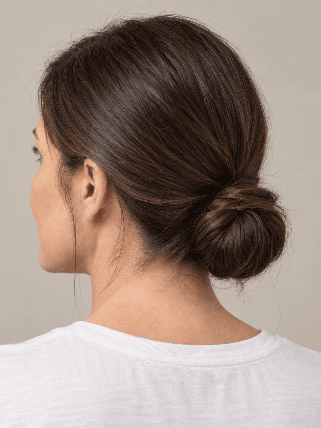 Sleek low bun on a woman with light skin and straight dark brown hair, close view of the bun from the back-left