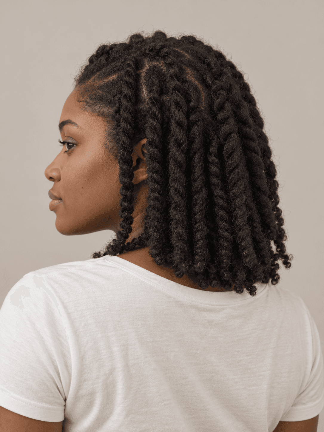 Two-strand twists on a woman with dark brown skin and coily hair, seen from the back-left to show the style