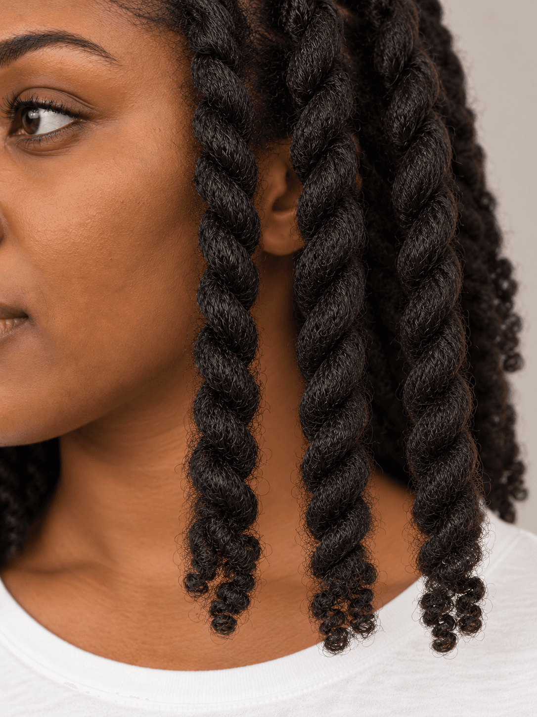 Two-strand twists on a woman with dark brown skin and coily hair, close view of three twists and their ends