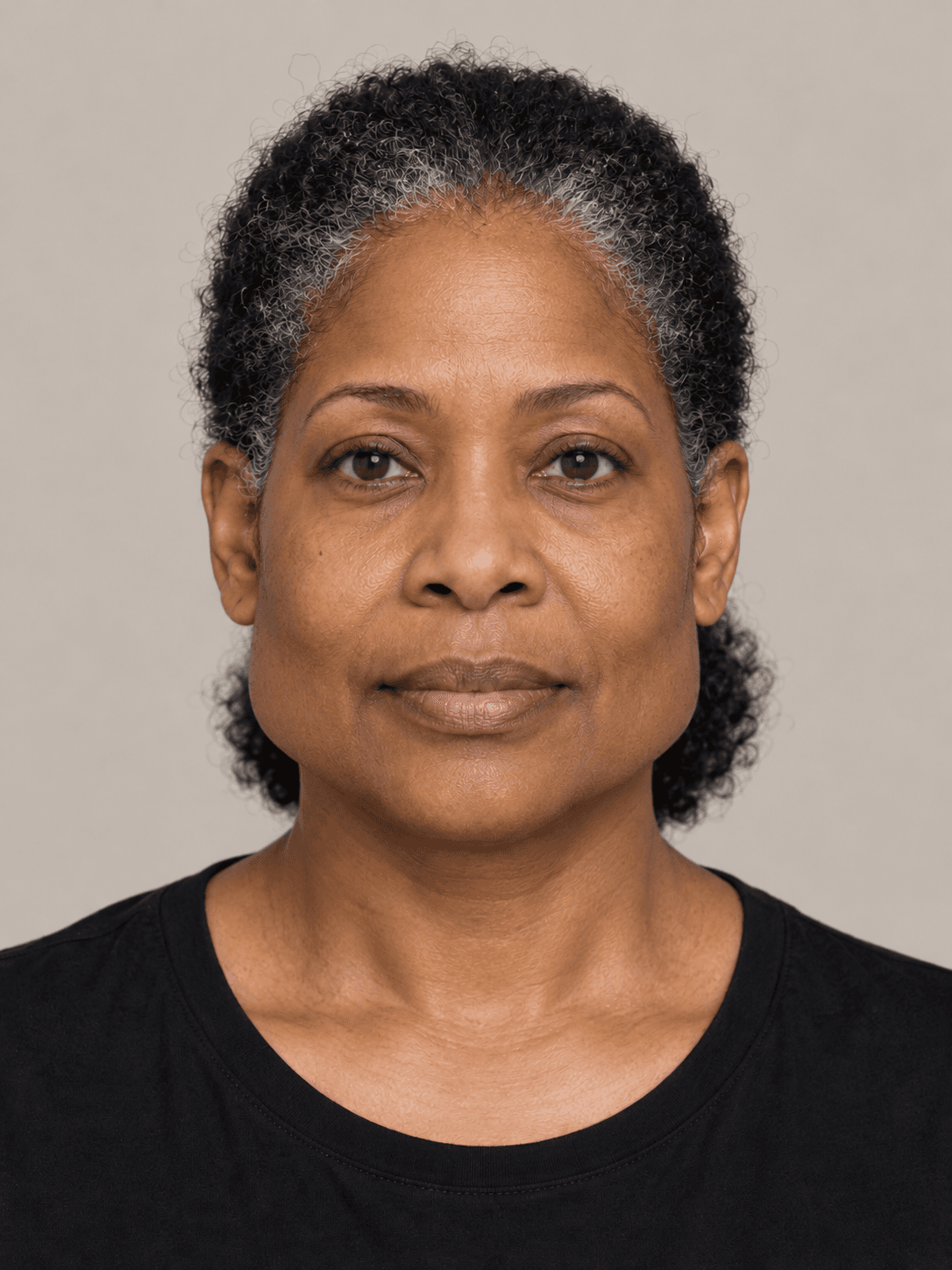Woman, front view, with deep brown skin and natural coily black hair, grey at the temples, pulled back in a low puff behind the head.
