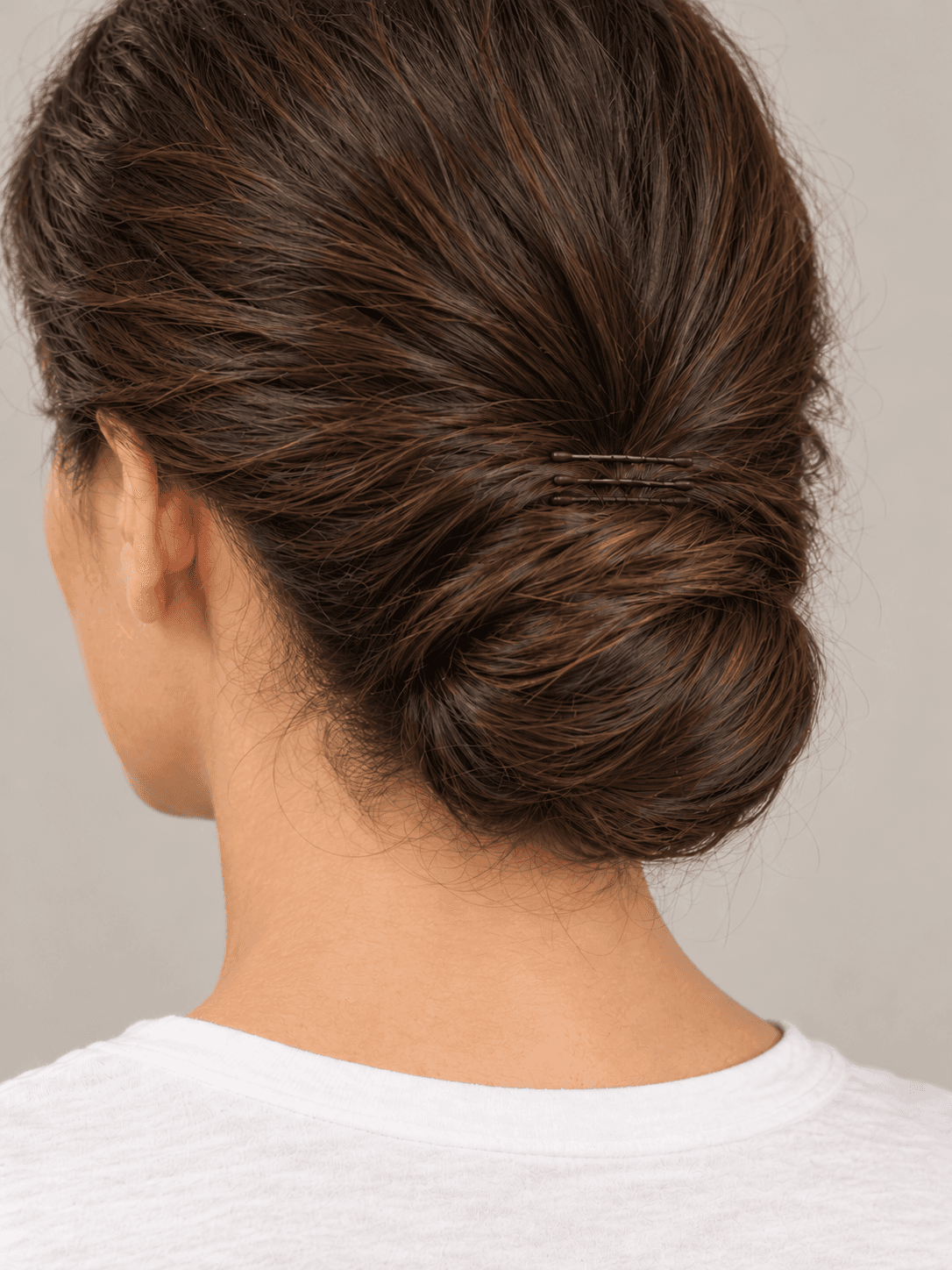 Low Chignon on a woman with light olive skin and dark brown hair, close view from the back-left of the chignon and the pin line above it